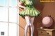 A woman in a green dress and white stockings leaning against a wall.