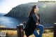 A woman sitting on a wooden fence by the ocean.